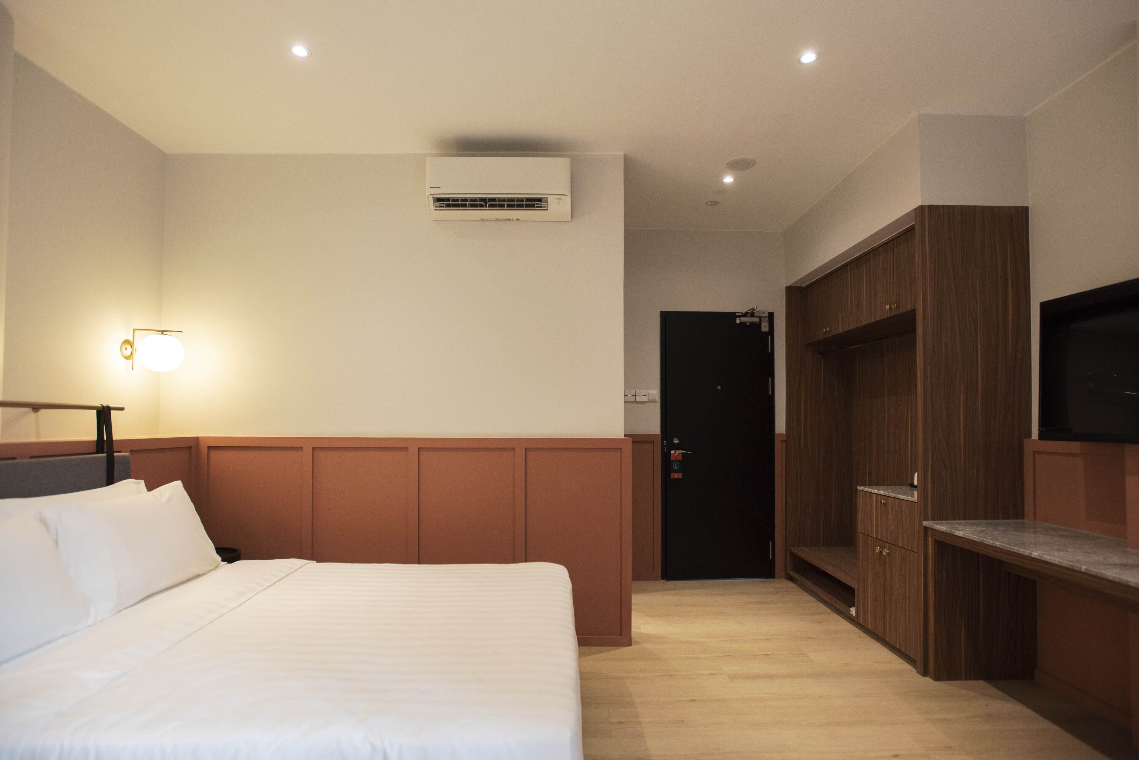 A hotel room with a bed, a wardrobe, a desk, and an air conditioning unit.