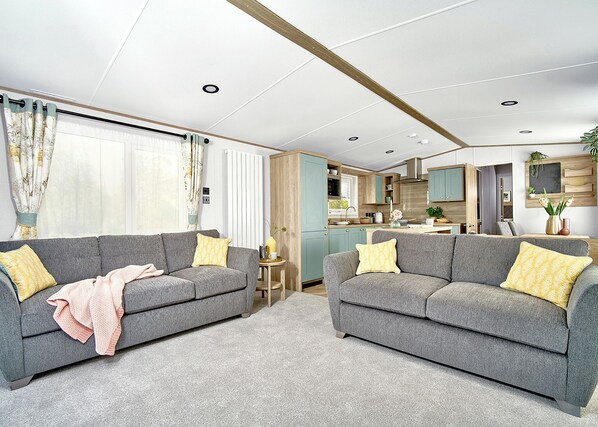 A modern living room with two grey sofas, a small side table, and a kitchen area visible through an open door.