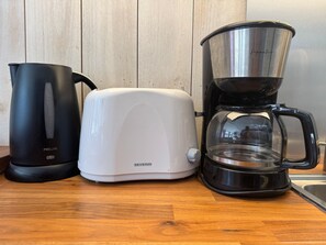 Een aanrecht met een zwarte elektrische waterkoker, een witte broodrooster en een zwarte koffiemachine.