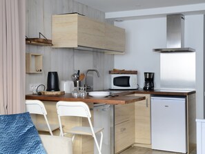 Een kleine keuken met houten kastjes, een magnetron, een koffiezetapparaat en een vaatwasser.