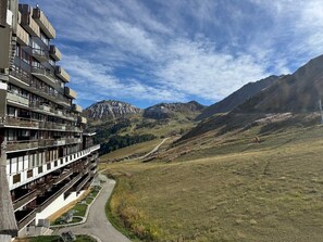 A multi-story hotel with balconies, a mountain view, and a pathway leading to a road.