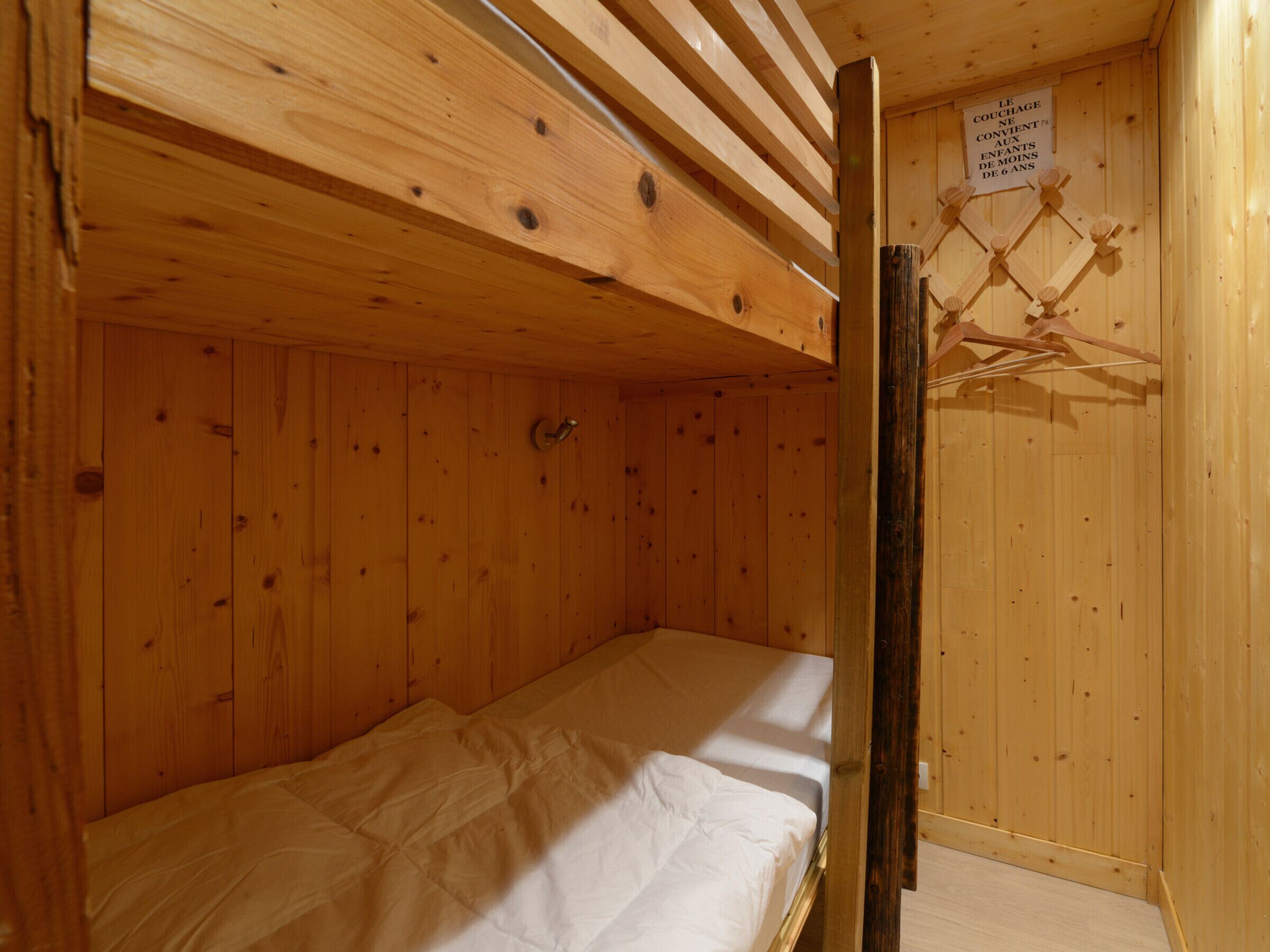 Una piccola stanza in legno con un letto a castello e un soffitto in legno. C'è un cartello appeso al muro e una rastrelliera di legno con vestiti.