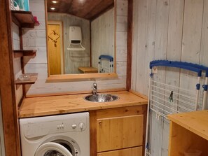 Ein kleines Badezimmer mit Waschtisch aus Holz, einem Waschbecken, einem Spiegel, einer Waschmaschine und einem Wäscheständer.