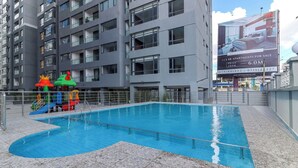 Una piscina con plataforma de baldosas, rodeada por un edificio de gran altura con múltiples balcones.