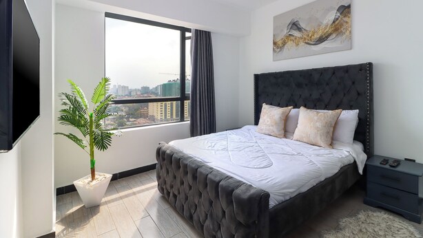 Un dormitorio moderno con una cama grande, una planta en maceta, una mesita de noche y vistas a la ciudad.