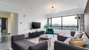 Una sala moderna con un televisor de pantalla plana, un conjunto de sofá, una mesa de centro y un amplio ventanal con vistas a la ciudad.