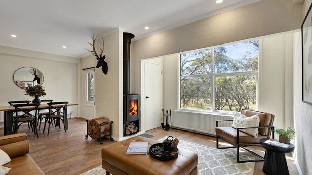 A cozy living room with a fireplace, wooden furniture, and a large window offering a view of trees. - Snowgums 17 - Dinner Plain (Dinner Plain)