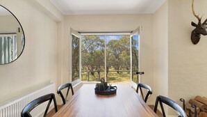 A dining area with a wooden table, four chairs, a mirror, and a deer head mounted on the wall. - Snowgums 17 - Dinner Plain (Dinner Plain)