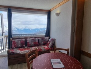 A room with a wooden bench and a table, a window with a view of mountains, and a wall-mounted light fixture.