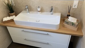 A bathroom with a white sink, two faucets, a wooden countertop, and a white cabinet with drawers. - Moderne Ferienwohnung mitten im Grünen in der Südeifel (Irrel)