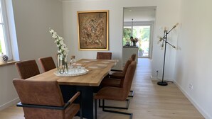A dining area with a long wooden table, brown upholstered chairs, a vase with white flowers, and a painting on the wall. - Moderne Ferienwohnung mitten im Grünen in der Südeifel (Irrel)