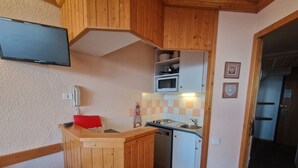 Une cuisine compacte avec des meubles en bois, un four à micro-ondes, un évier et un téléviseur fixé au-dessus du plan de travail.
