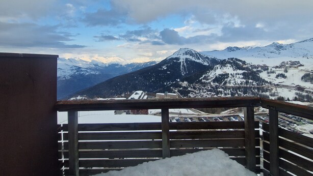 Une vue sur les montagnes depuis un balcon doté d’une balustrade en bois, un paysage enneigé et des montagnes lointaines.