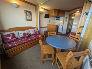Een gezellig interieur met een bank, een houten eettafel, stoelen en een kitchenette.