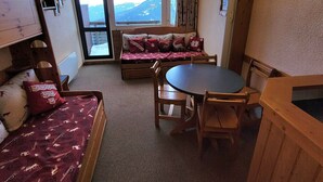 Une pièce confortable avec un lit, un canapé, une table à manger et une vue sur les montagnes, visible à travers une grande fenêtre.