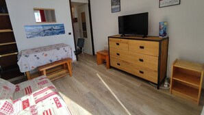 Ein kleiner, ordentlicher Raum mit einem Bett, einem Schminktisch, einem Fernseher und einer Tür zu einem anderen Raum.