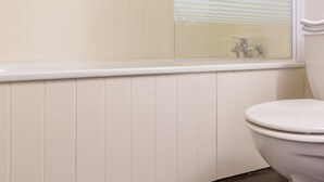 Ein Badezimmer mit Toilette, einem Fenster mit Jalousien und einer weißen Badewanne.