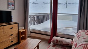 Ein Zimmer mit einem Holzkoffer, einem Fernseher, einem Fenster mit Blick auf eine verschneite Landschaft und einem roten Vorhang.