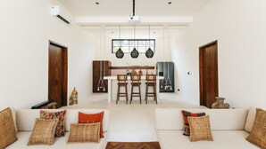 A spacious living room with a sofa set, a dining area with a table and chairs, and a kitchen in the background. - Villa Lamer (Canggu)