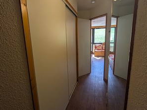 Um corredor estreito com piso de madeira que leva a um quarto com cama e janela.