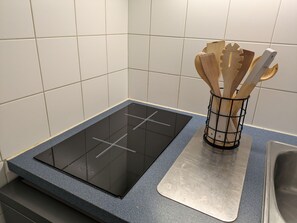 A kitchen with a black induction cooktop, a stainless steel sink, and a wooden utensil holder on a blue countertop.