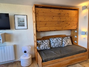 A cozy room with a wooden bed, a white radiator, a white bear-shaped stool, and a framed picture on the wall.