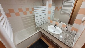 A bathroom with a white bathtub, a glass shower enclosure, a granite countertop sink, and a mirror above the sink.