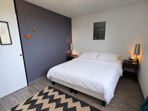 A bedroom with a bed, two bedside tables, a wall-mounted lamp, a door, and a rug.
