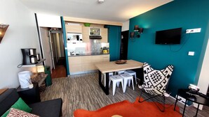 A compact living space with a kitchenette, a dining area, and a seating area with a sofa and ottoman.