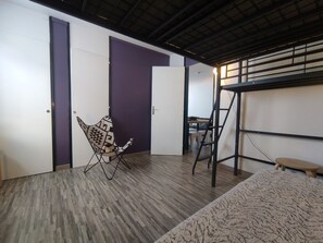 Una habitación con una cama nido, una silla plegable y un escritorio con silla.