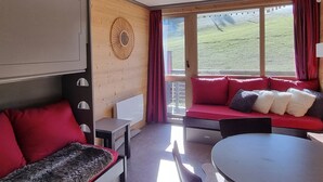 A modern room with a sofa, a table, and a large window offering a view of a grassy area. - Cozy studio with direct slope access, slope view, pets allowed (Plagne Aime 2000)