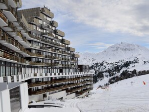 A multi-story hotel with balconies and a ski slope in the background.