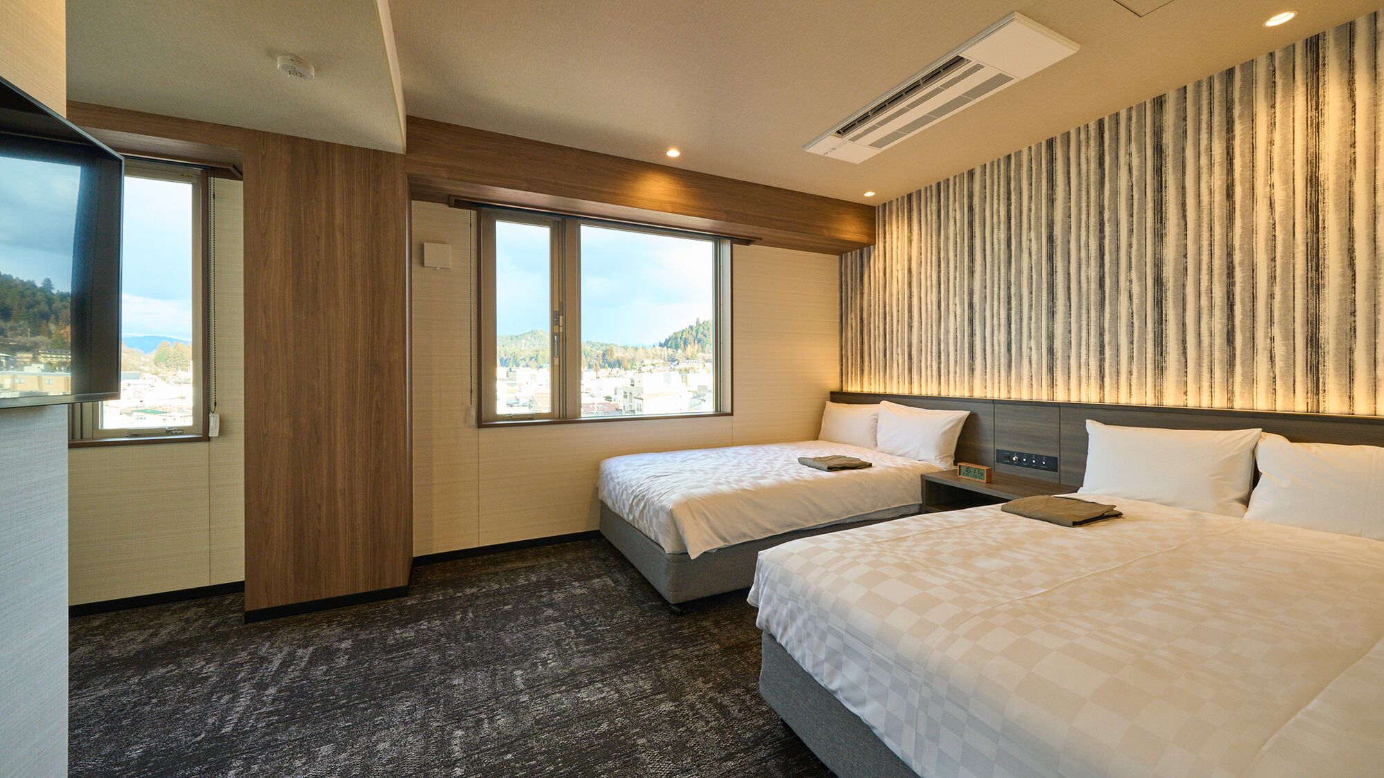 Une chambre d’hôtel avec deux lits, une grande fenêtre, un climatiseur fixé au mur et une vue sur le paysage urbain.