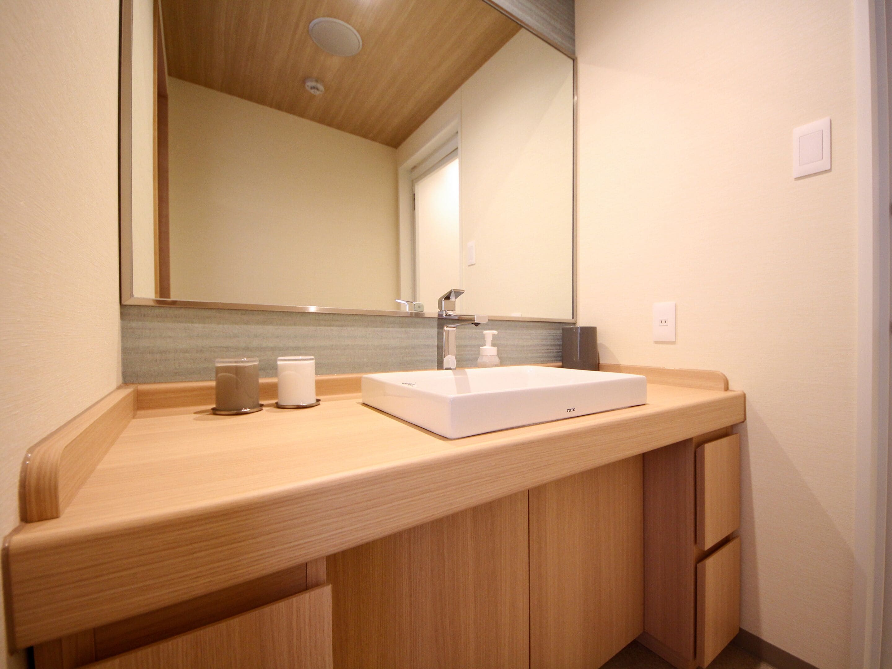 Un baño moderno con tocador de madera, un lavabo blanco y un espejo grande.
