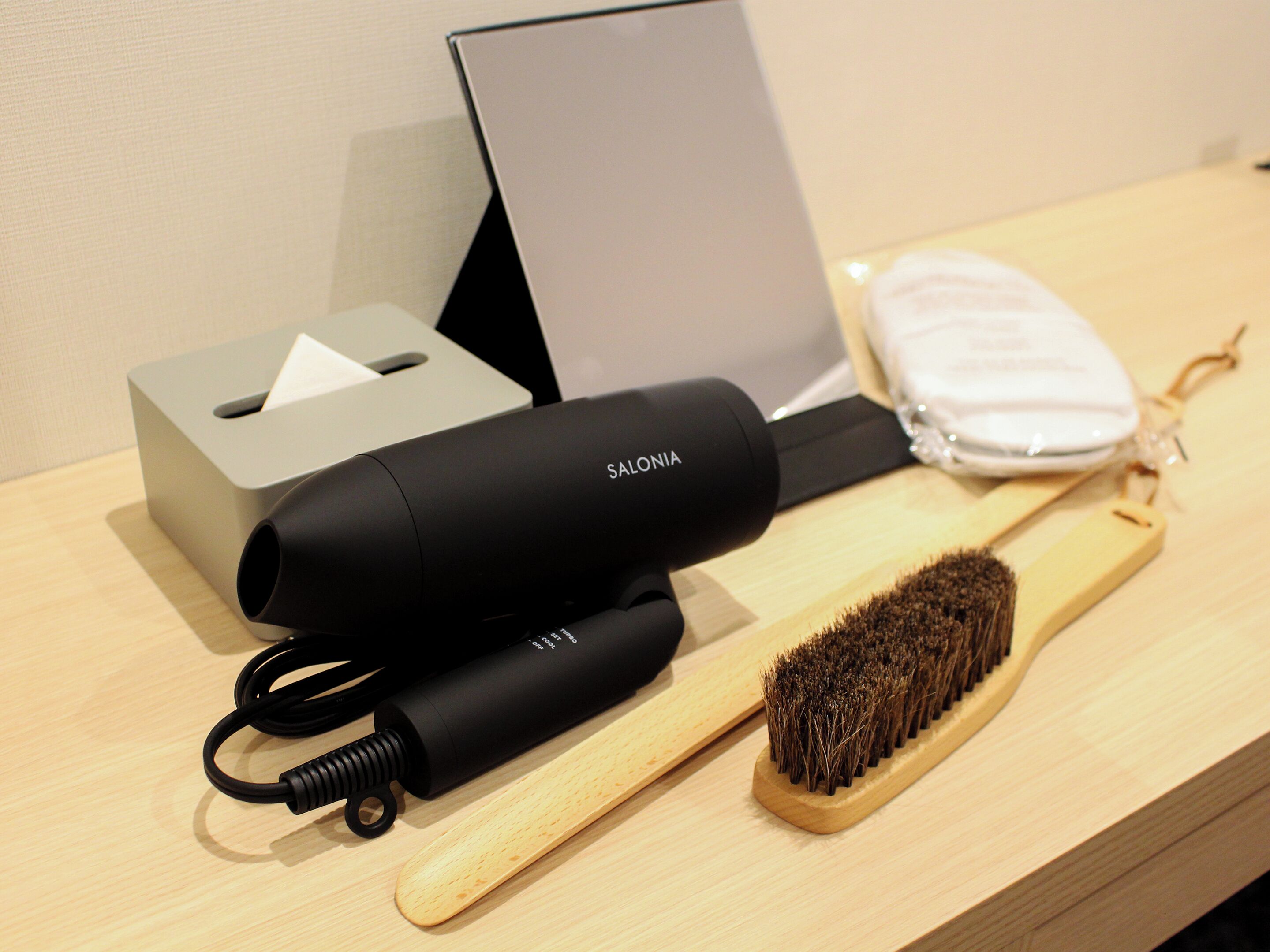 A hairdryer, a wooden brush, a tissue box, and a small white bag on a wooden surface.