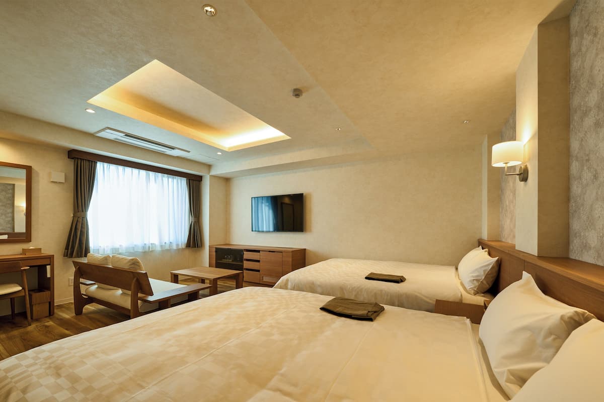 Habitación de hotel con dos camas, un escritorio, una silla, un televisor y una ventana con cortinas.