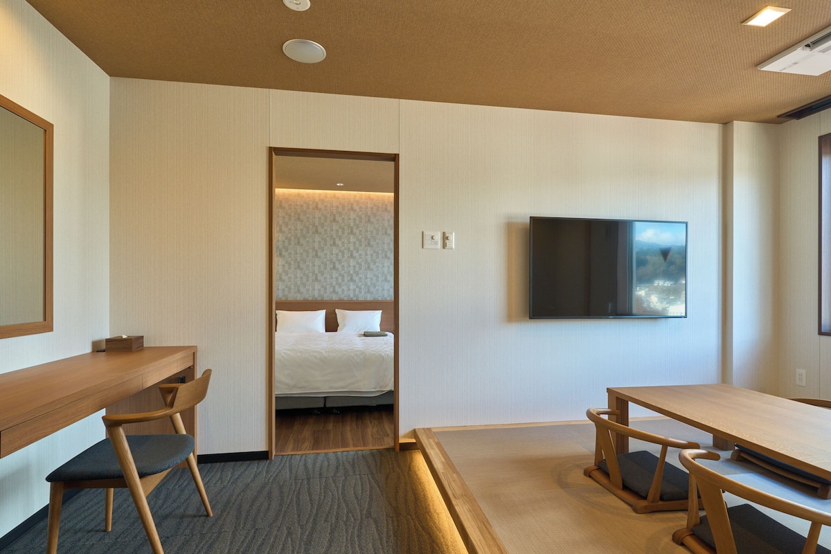 Habitación de hotel con cama, escritorio, silla, televisor y una mesita.