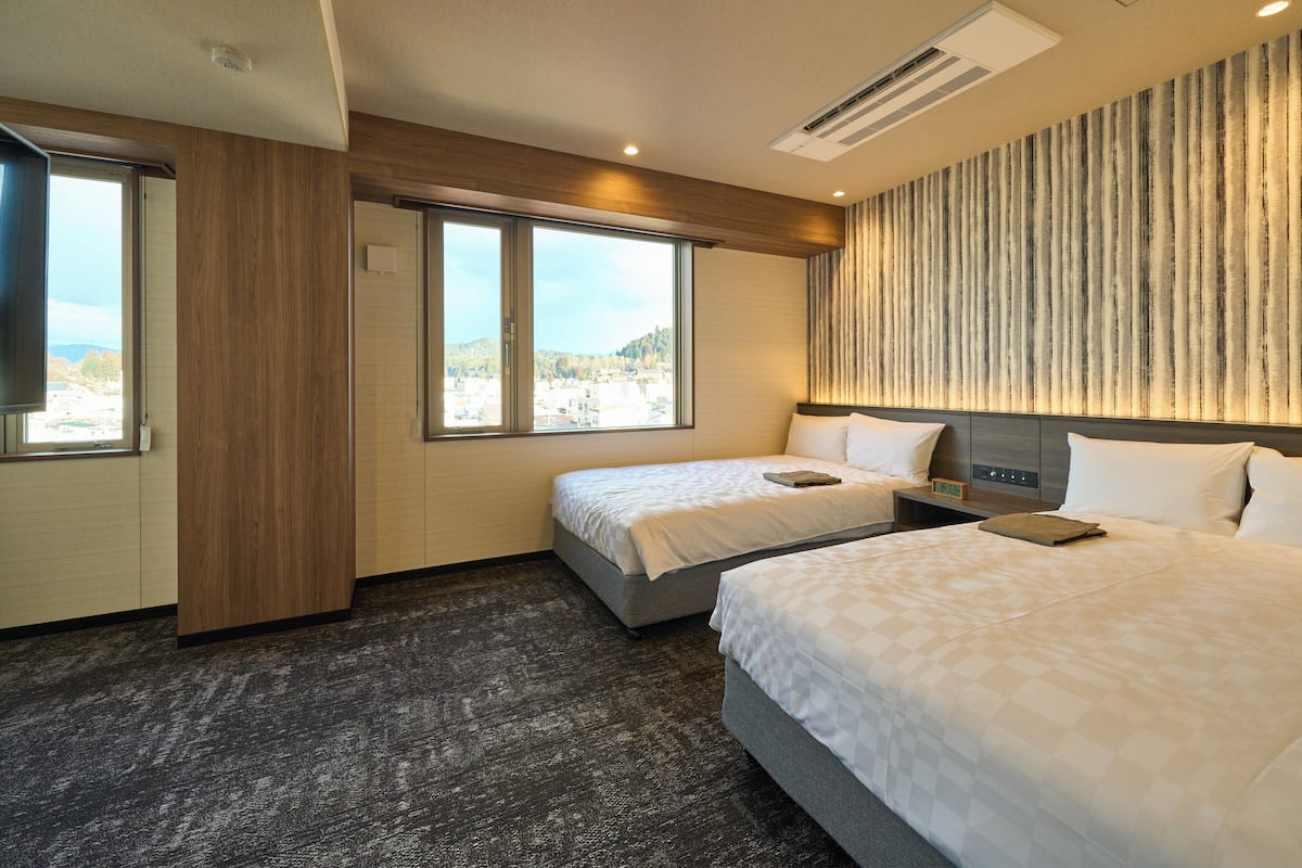 Habitación de hotel con dos camas, un ventanal con vistas, aire acondicionado instalado en la pared y un televisor de pantalla plana.
