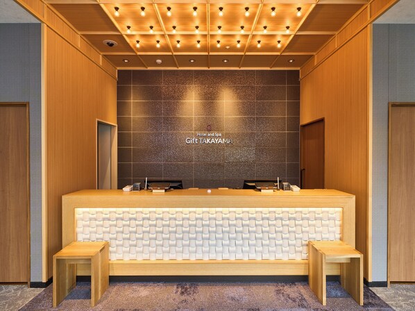 Una recepción de hotel con diseño moderno, una pared de azulejos oscuros y un cartel que dice 'Hotel and Spa Gift TAKAYAMA'.