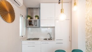 Een moderne keuken met witte kasten, een roestvrijstalen spoelbak en een ingebouwde oven. Er staan twee groene stoelen bij de tafel en een decoratief kunstwerk boven de oven.