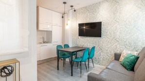 Een moderne woonkamer met een grijze bank, blauwgroene stoelen en een flatscreen televisie aan de muur.