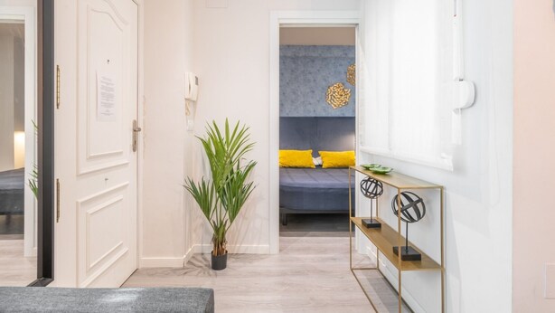 Een moderne hotelkamer met een bed, een nachtkastje, een potplant en een console met decoratieve objecten.