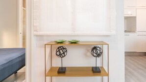 Een moderne hotelkamer met een bed, een console met decoratieve objecten, en uitzicht op de keuken.