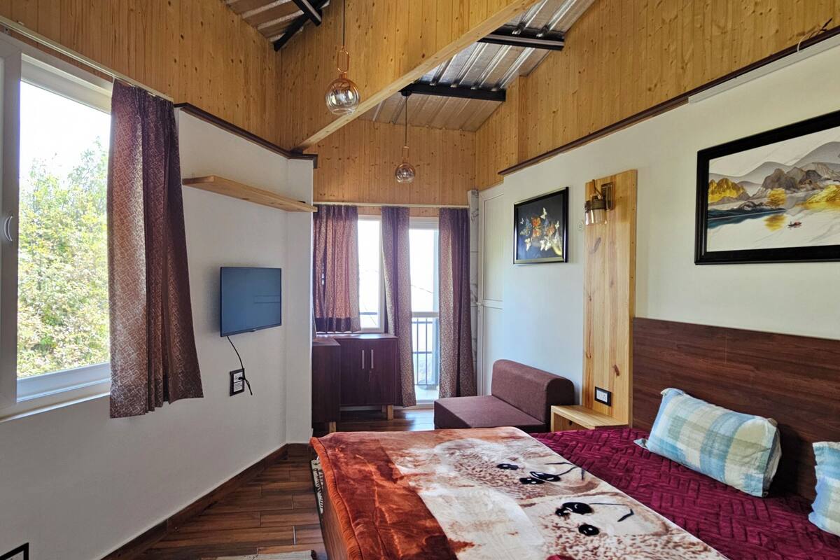 Ein Schlafzimmer mit Holzbalkendecke, einem Bett mit gemustertem Überwurf, einem angebrachten Fernseher und einem Gemälde an der Wand.