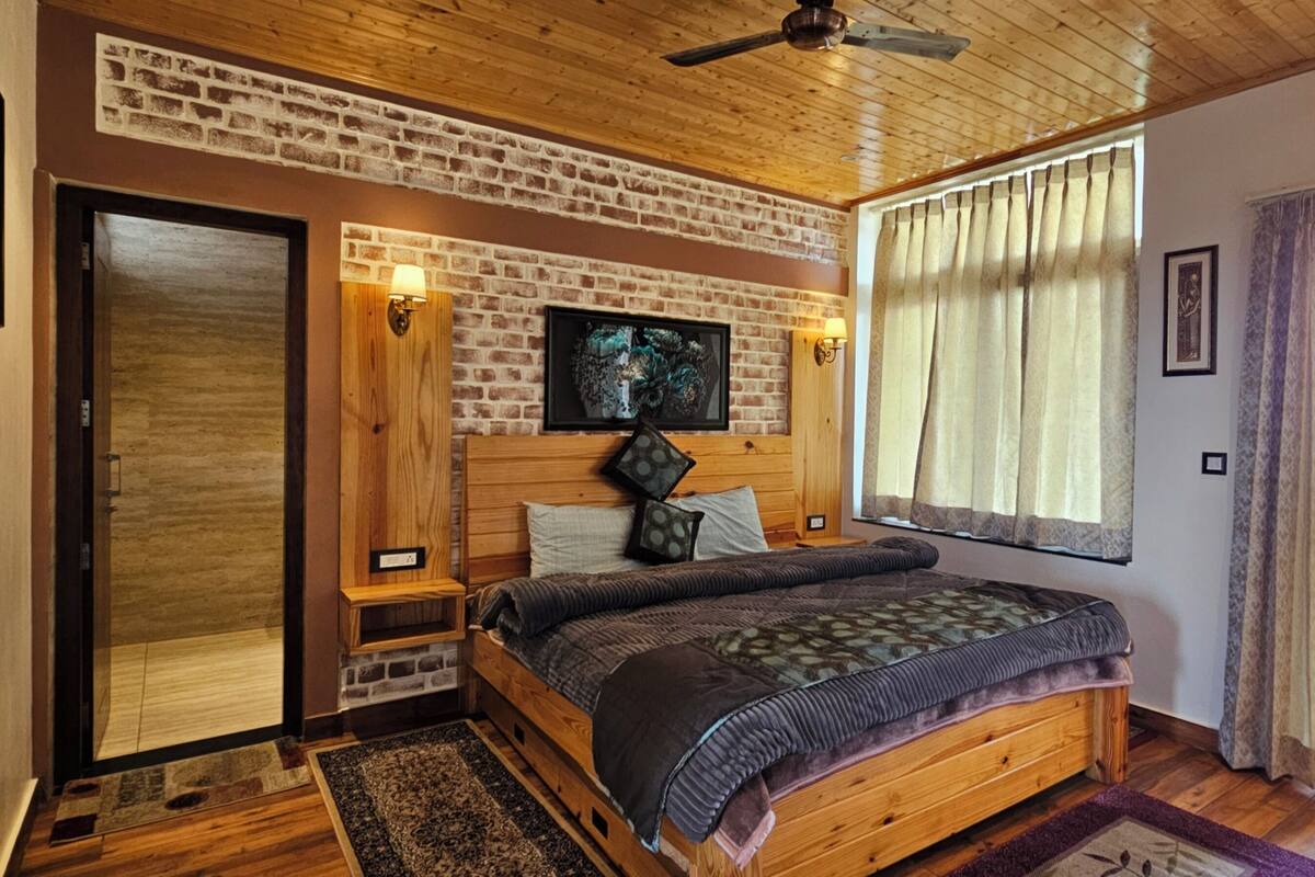 Ein Schlafzimmer mit einem hölzernen Bett, einem Fernseher, einer Ziegelwand und einem Balkon mit Vorhängen.