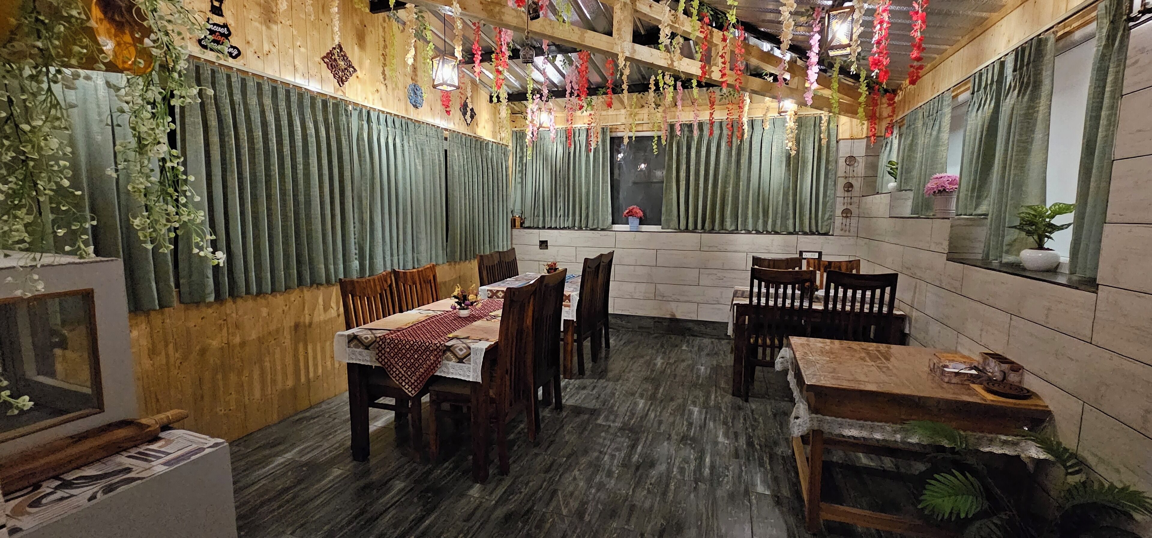 A restaurant with wooden walls, green curtains, and hanging floral decorations.