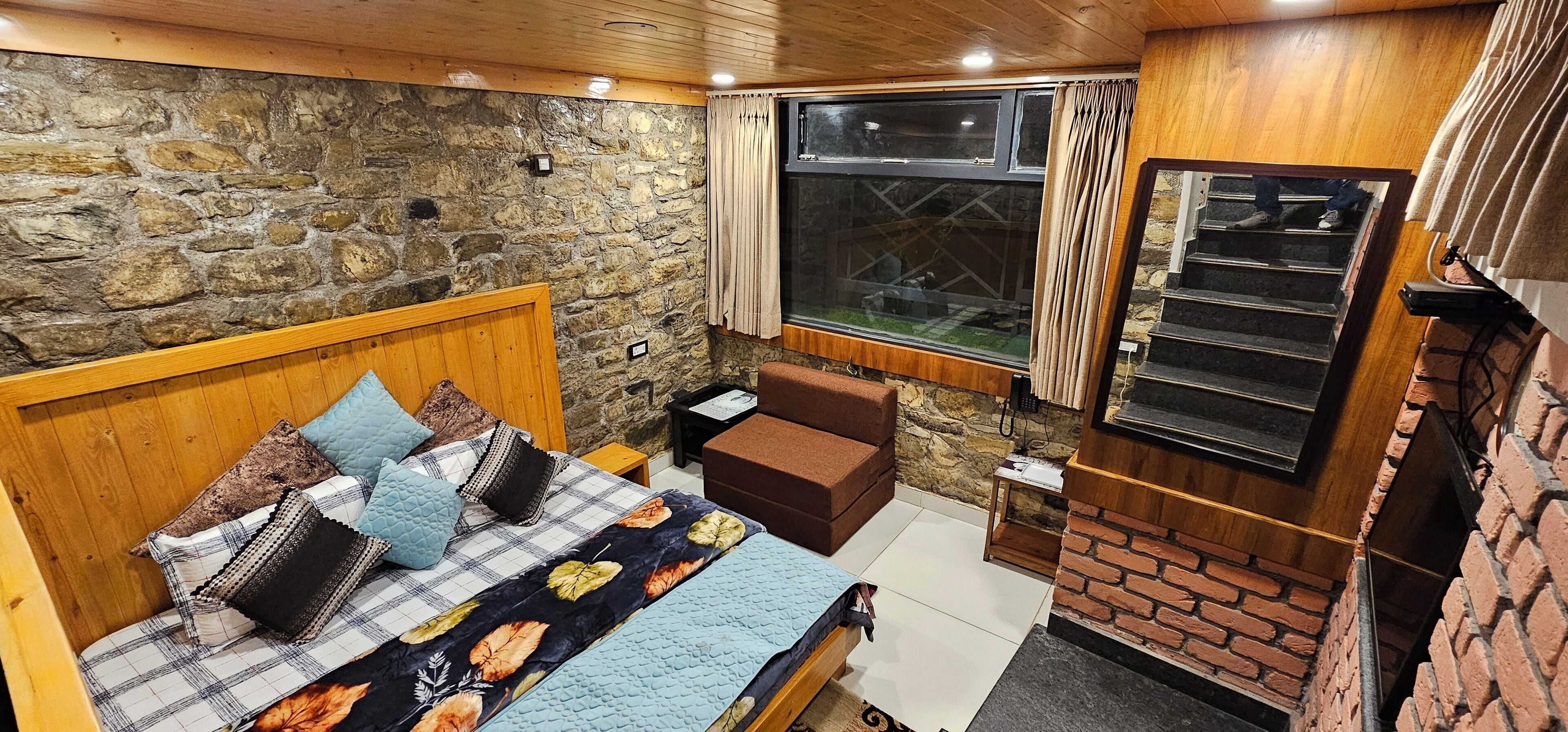A bedroom with a stone wall, a wooden bed, a small sofa, a TV, and a window with curtains.