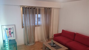 A living room with a red sofa, a wooden coffee table, and sheer curtains.