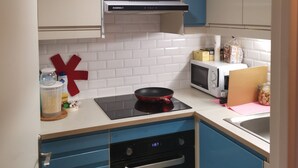 A kitchen with blue and white cabinets, a microwave, a stove, and a red cross decoration on the wall.