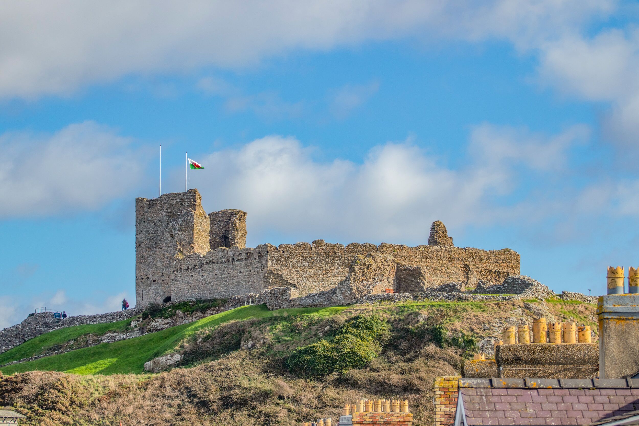 Un château historique, avec un drapeau, des ruines et une colline verdoyante.